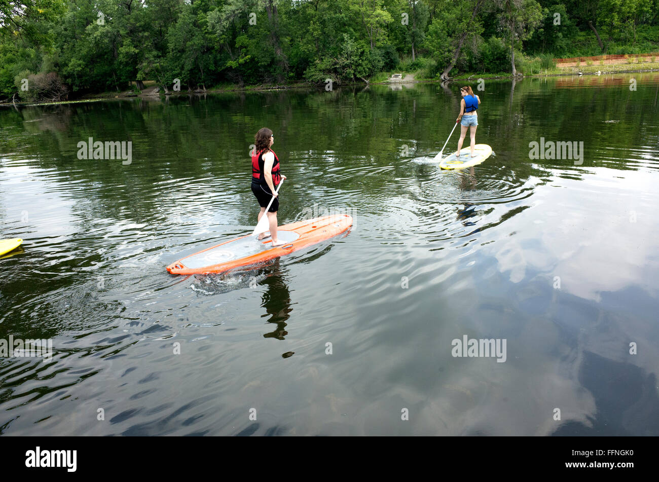 Teen women on stand-up paddleboards traversing channel between Lake Calhoun and Lake of the Isles. Minneapolis Minnesota MN USA Stock Photo