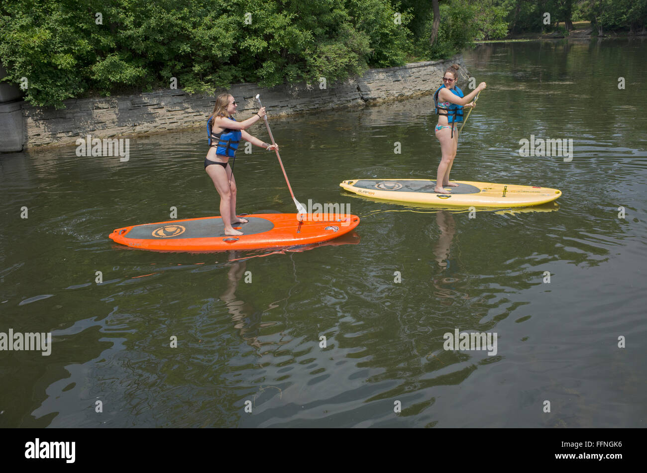 Teenage women on paddleboards paddling between Lake Calhoun and Lake of the Isles with life vests. Minneapolis Minnesota MN USA Stock Photo