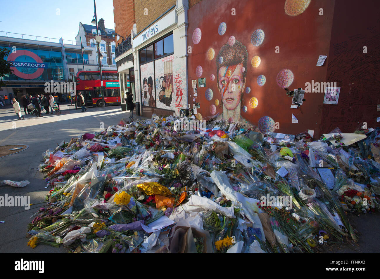 Flowers left under a David Bowie 'Aladdin Sane' mural on a street wall in Brixton, made into a makeshift shrine after his death. Stock Photo