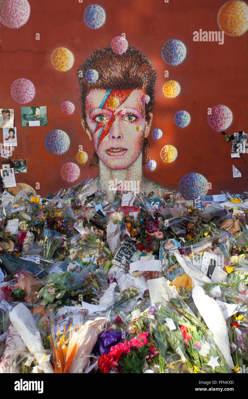 Flowers left under a David Bowie 'Aladdin Sane' mural on a street wall in Brixton, made into a makeshift shrine after his death. Stock Photo