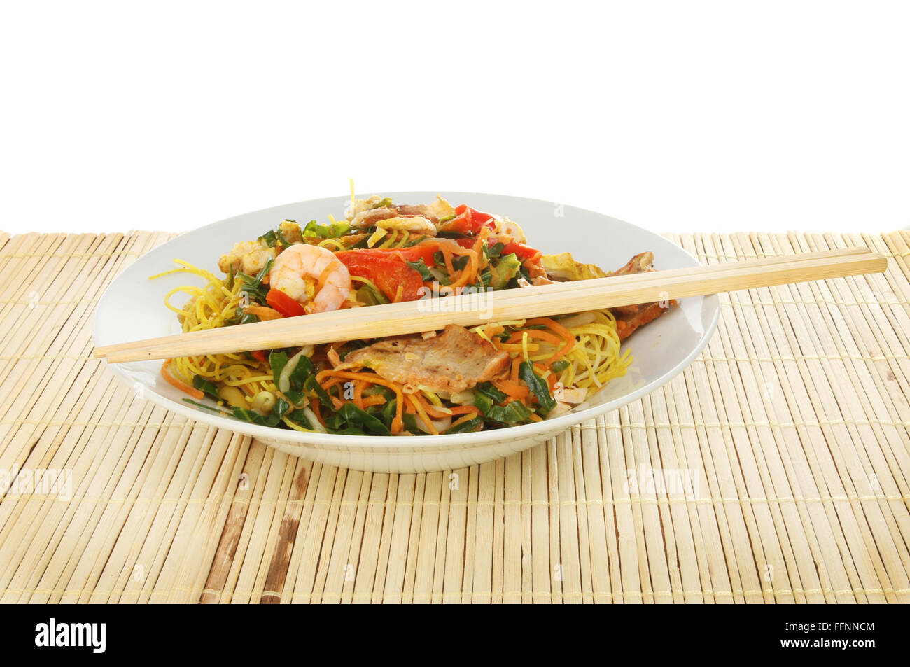 Chinese meal, Singapore noodles in a bowl with chopsticks on a bamboo matt Stock Photo