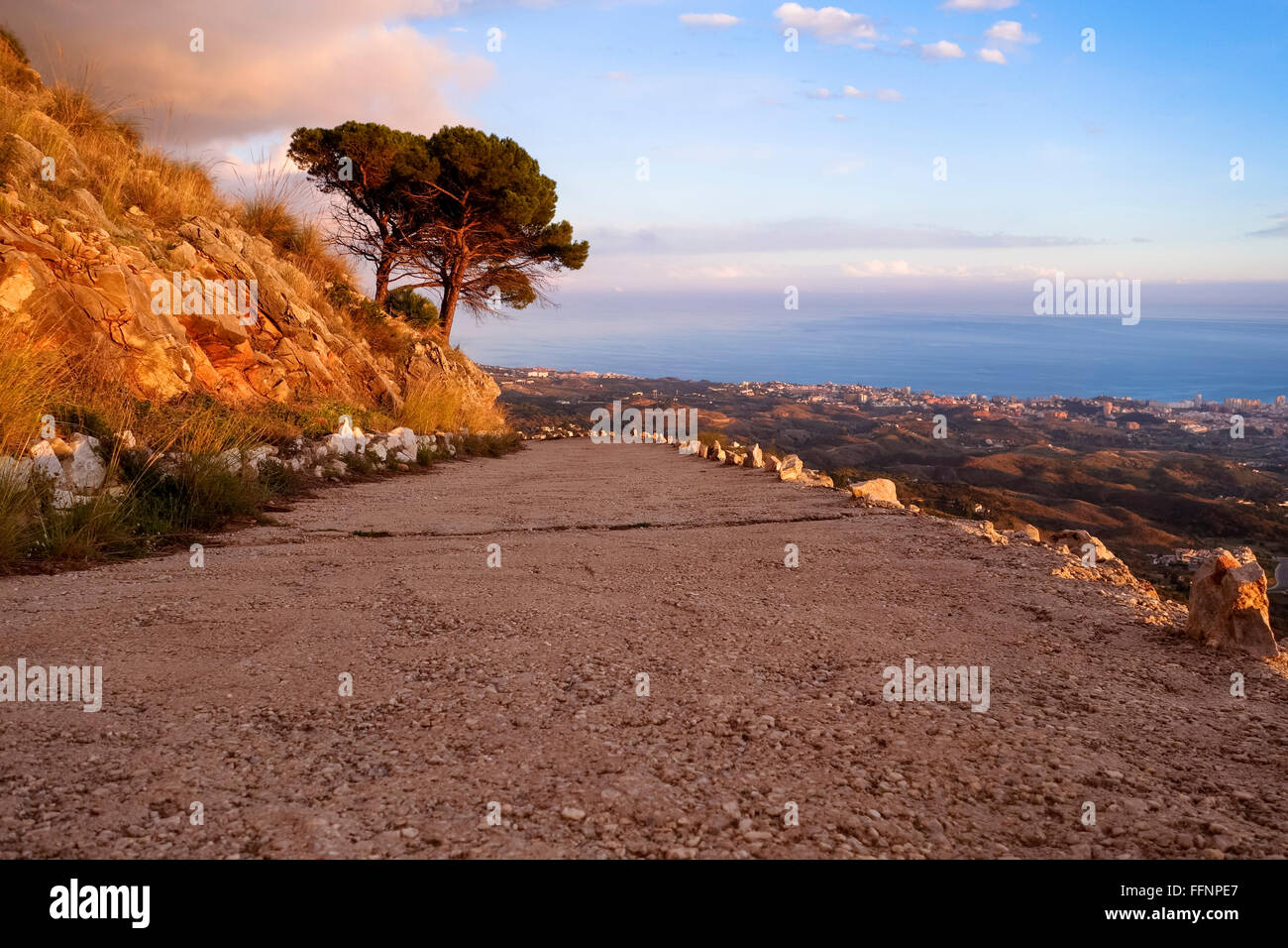 Concrete road in mountain area with Aleppo trees, no crash barrier during beautiful sunset. MIjas, Spain. Stock Photo