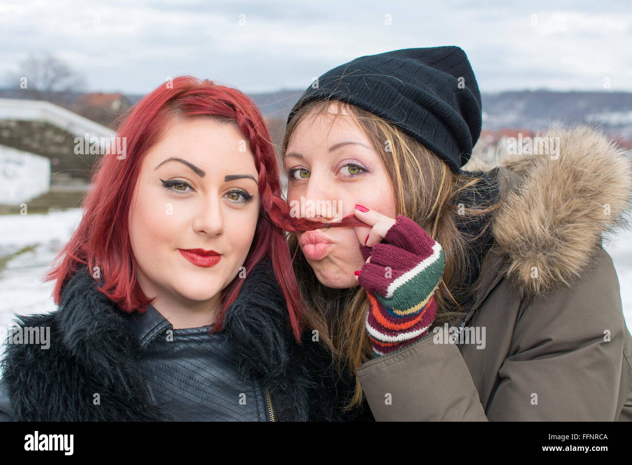 two girls having fun in the winter weather, one girl is making a mustache with her hair Stock Photo