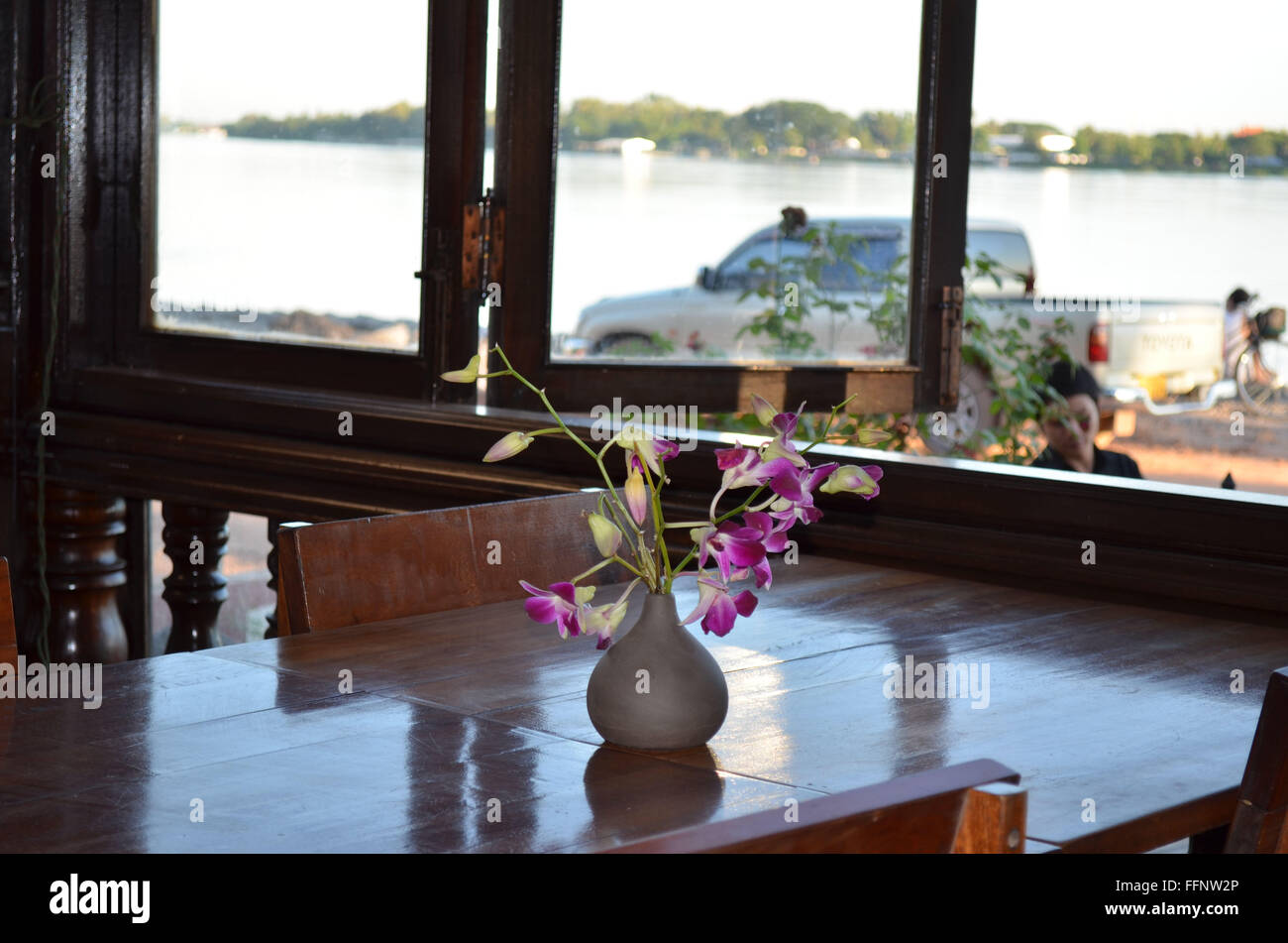 Purple orchids in vase on shiny table in cafe along Mekong River Stock Photo