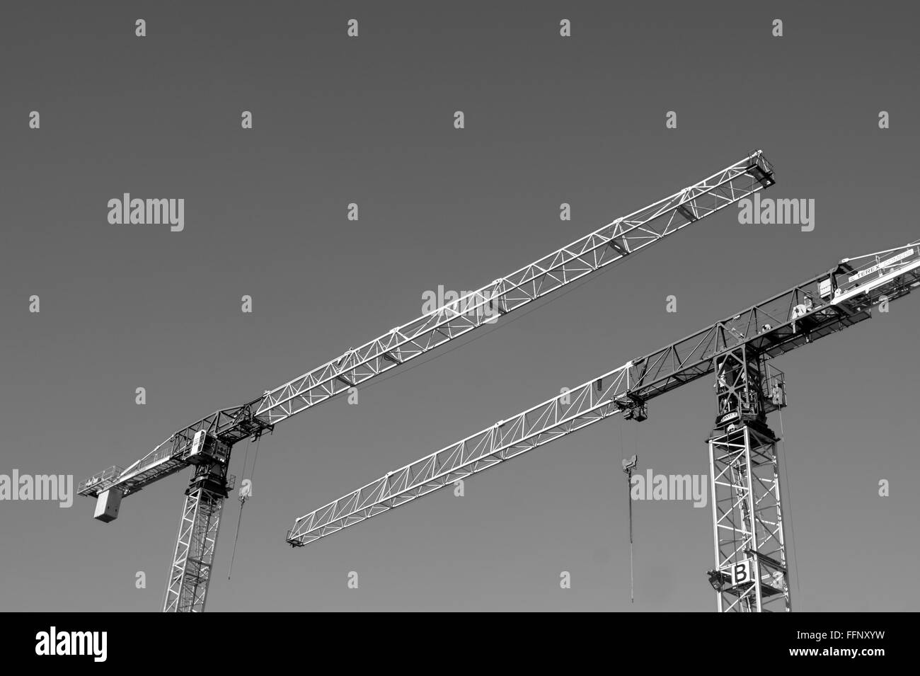 Black and white image of two tower construction cranes pointing in opposite directions against a clear sky Stock Photo