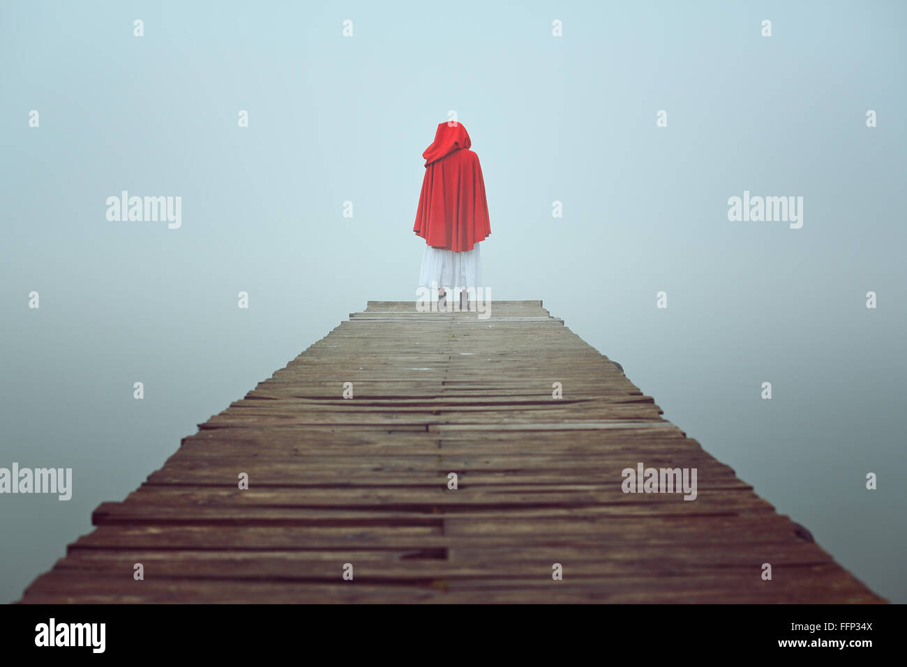 Red hooded woman looks at foggy lake on a wooden pier . Sadness and loneliness concept Stock Photo