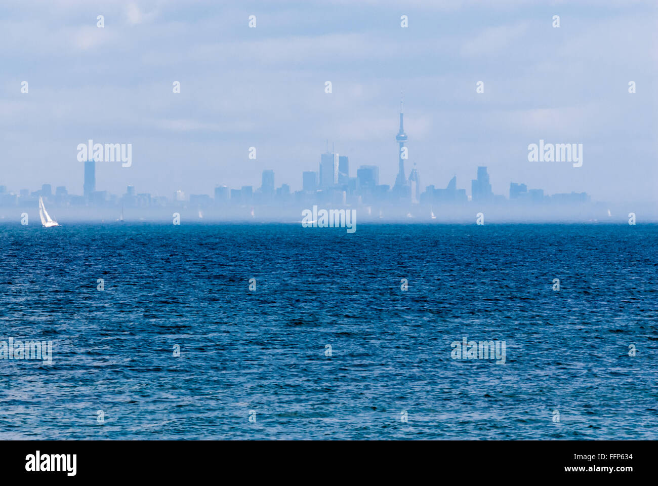 Toronto city skyline from across wavy blue rippled water with sailboat and other boats in distance in hazy fog. Stock Photo