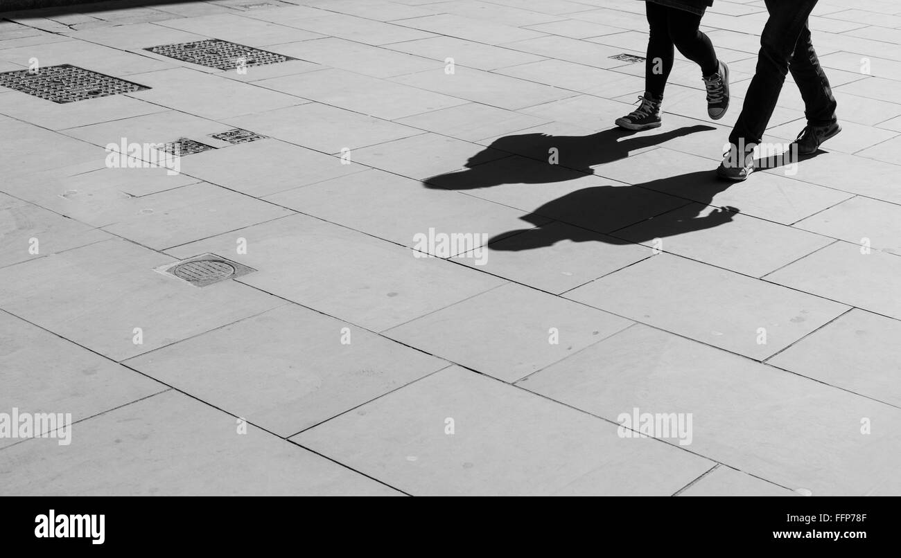 Shadows of two walking pedestrians projected on the sidewalk. Black and white. Stock Photo