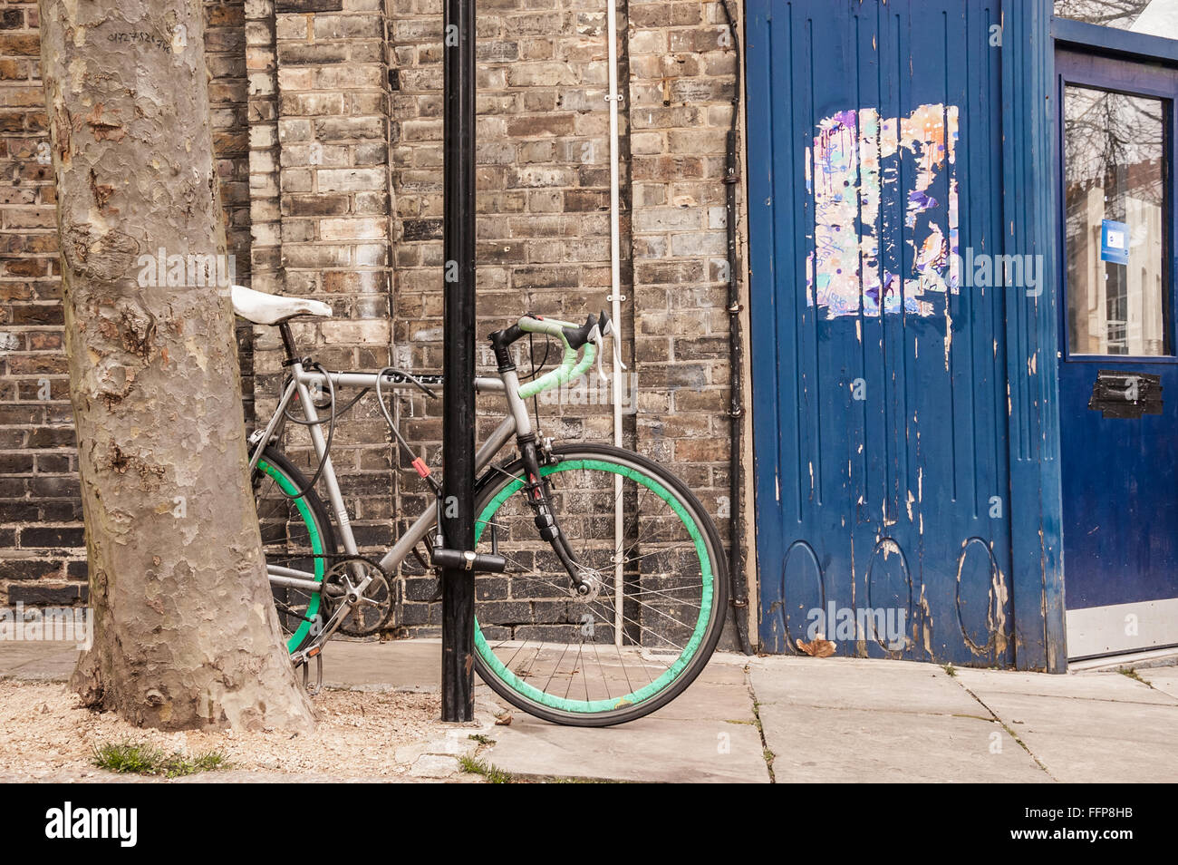 Cool single gear road bicycle locked to a street lamp in front of a stone wall and a blue pub door. Stock Photo