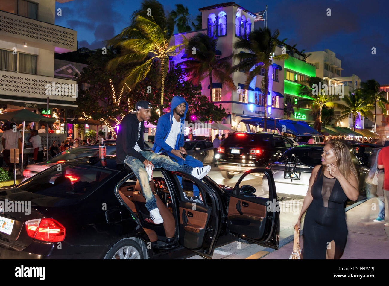 Florida South,Miami Beach,Ocean Drive,night evening,Black adult,adults,man men male,friend,sitting top car,passing,adult adults,woman female women,FL1 Stock Photo