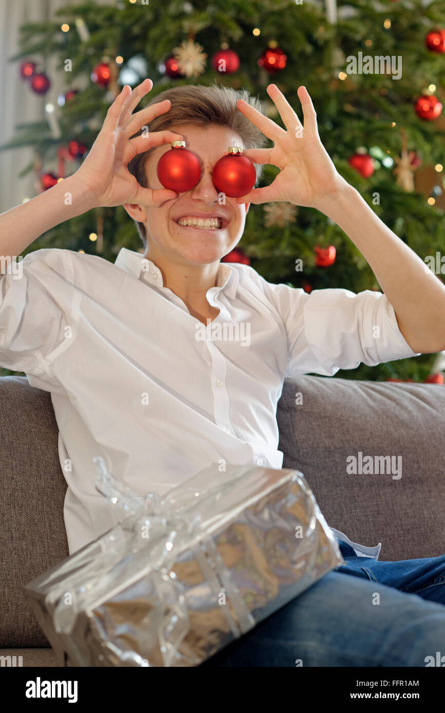 Young man, teenager with red baubles in front of eyes, Christmas, Germany Stock Photo