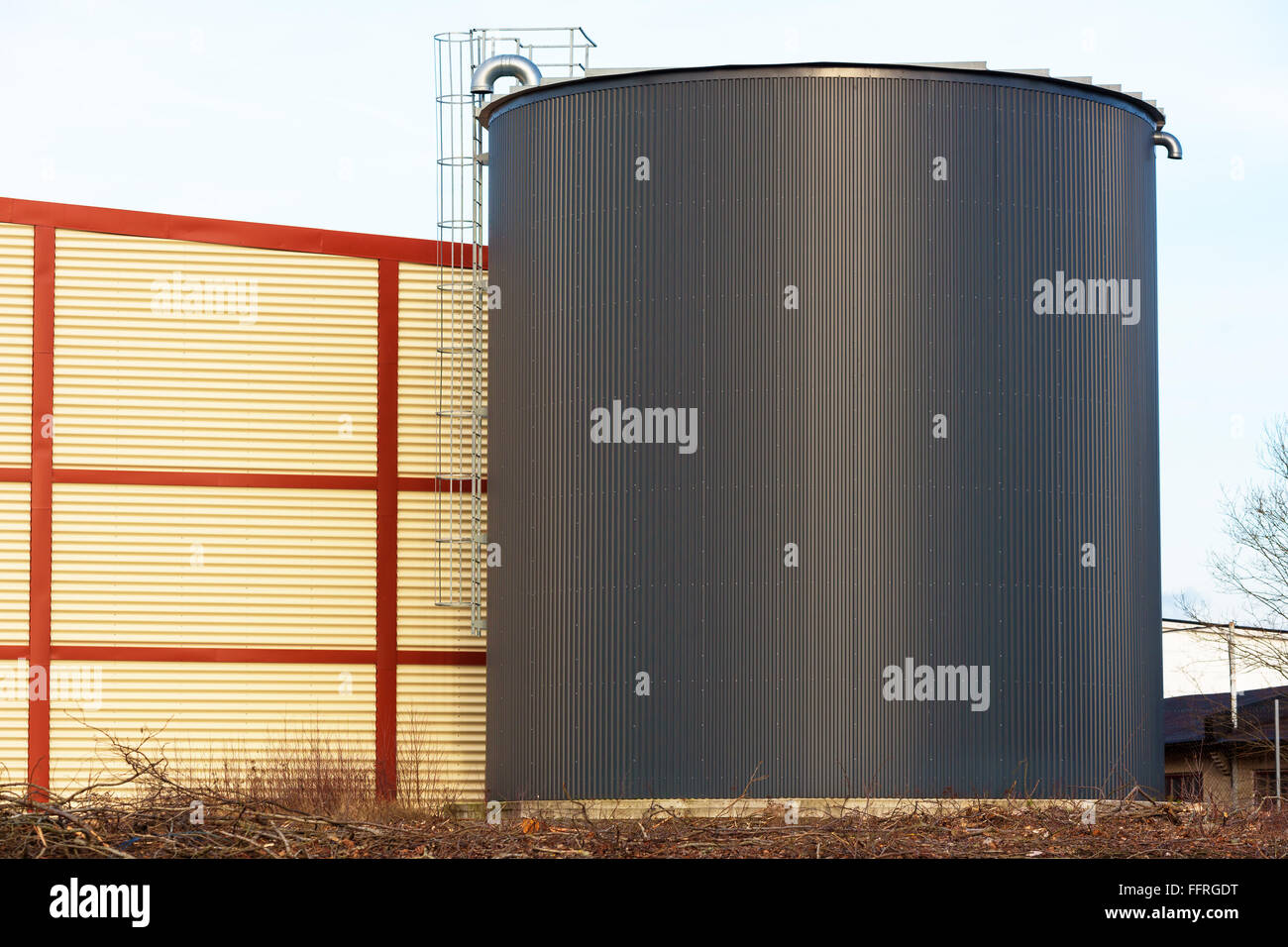 Large black silo or storage building with an aluminum or steel ladder on the outside. Red and yellow building behind ladder. Stock Photo