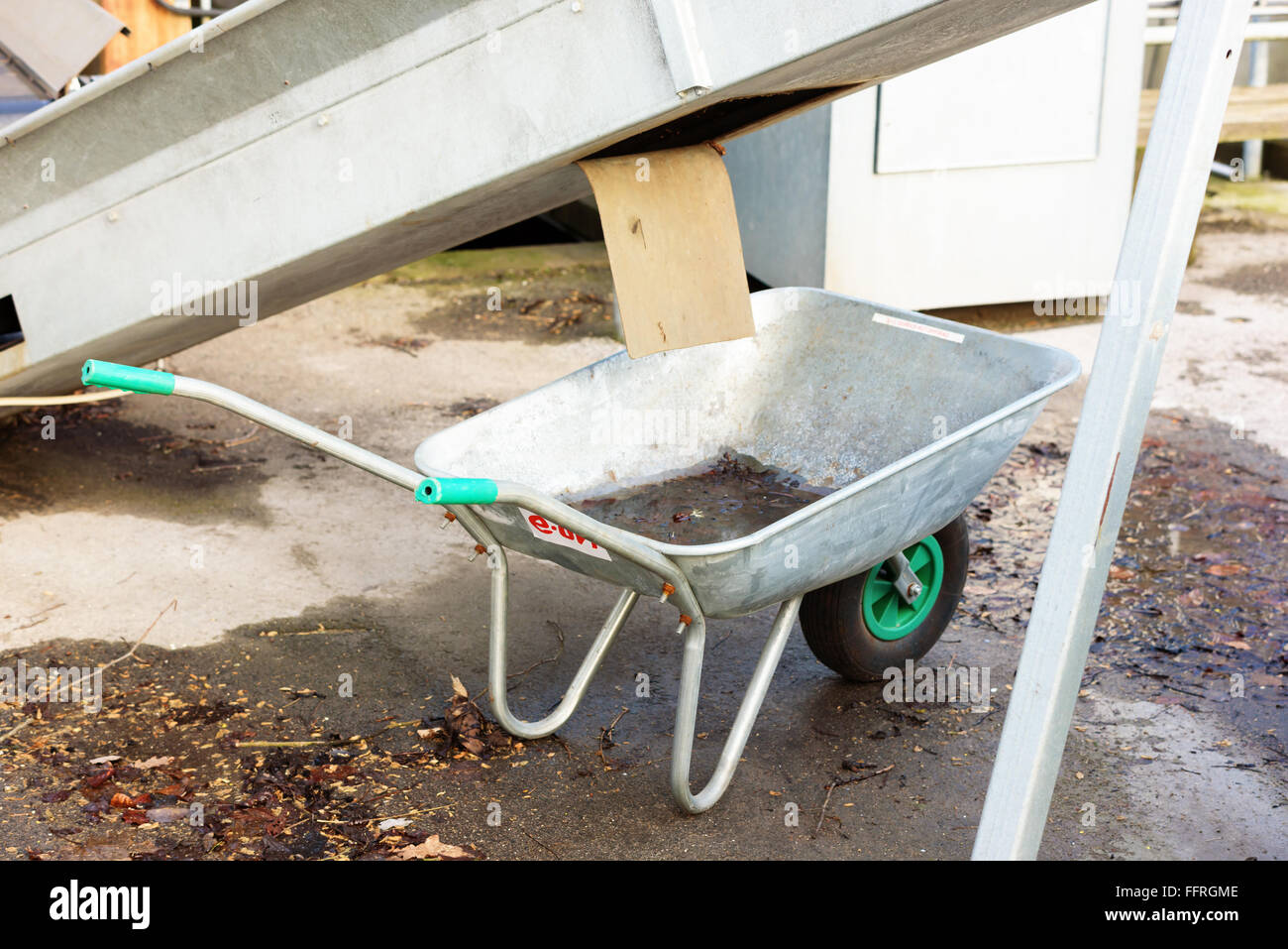 Kallinge, Sweden - February 07, 2016: An empty metal wheelbarrow stand under a conveyor belt waiting to get filled up. Some kind Stock Photo