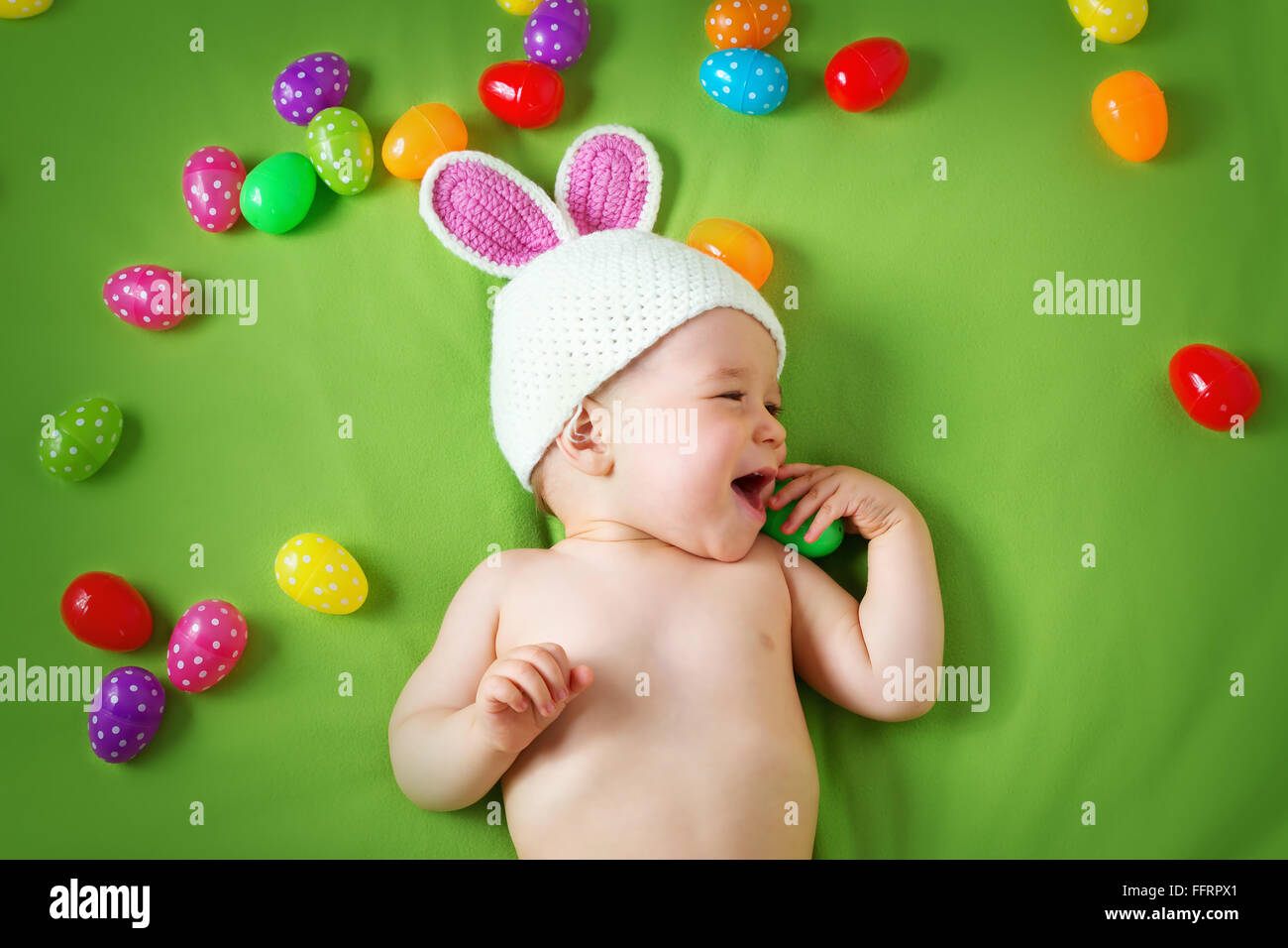 Baby boy in bunny hat lying on green blanket with easter eggs Stock