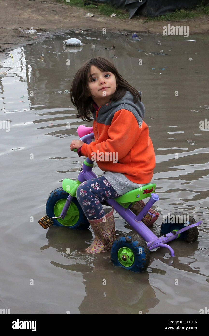 Portrait of a refugee girl (5 years) from Syria on her tricycle in puddle, she now lives with her parents in a tent camp near Calais, France Stock Photo