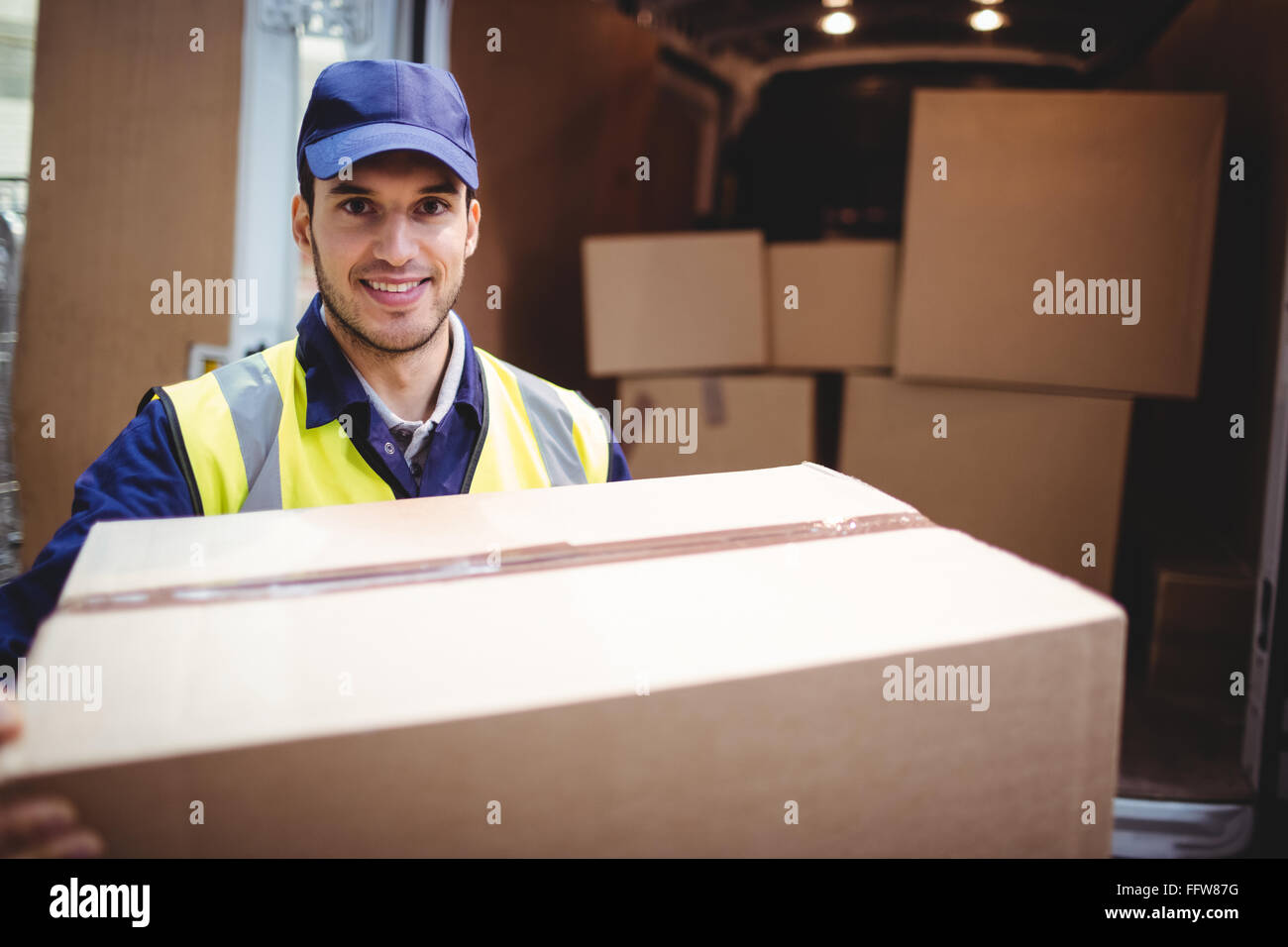 Delivery driver smiling at camera by his van holding parcel Stock Photo