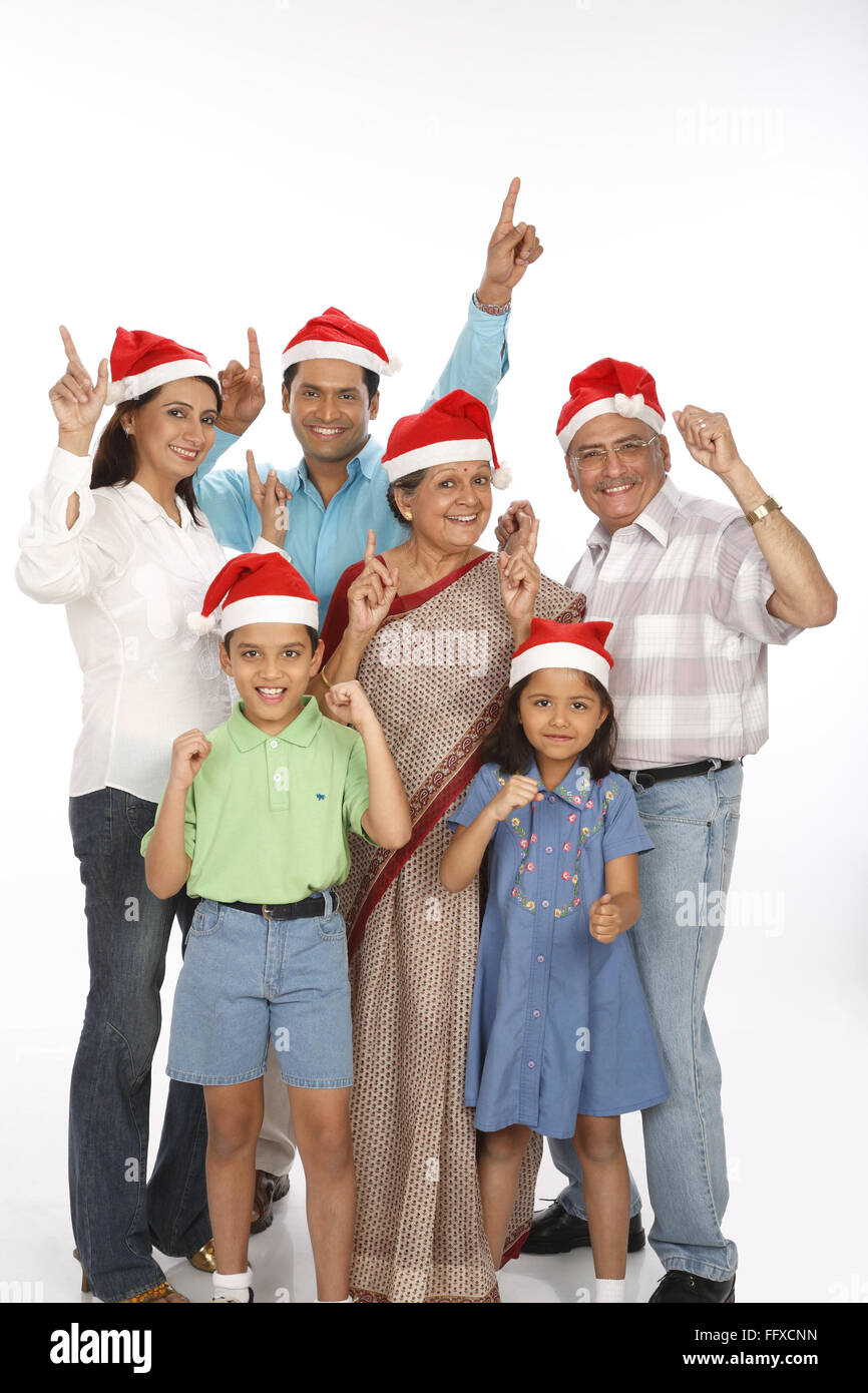 Parent children with grandparent wearing Santa clause caps raising hands with index finger pointing upwards Stock Photo