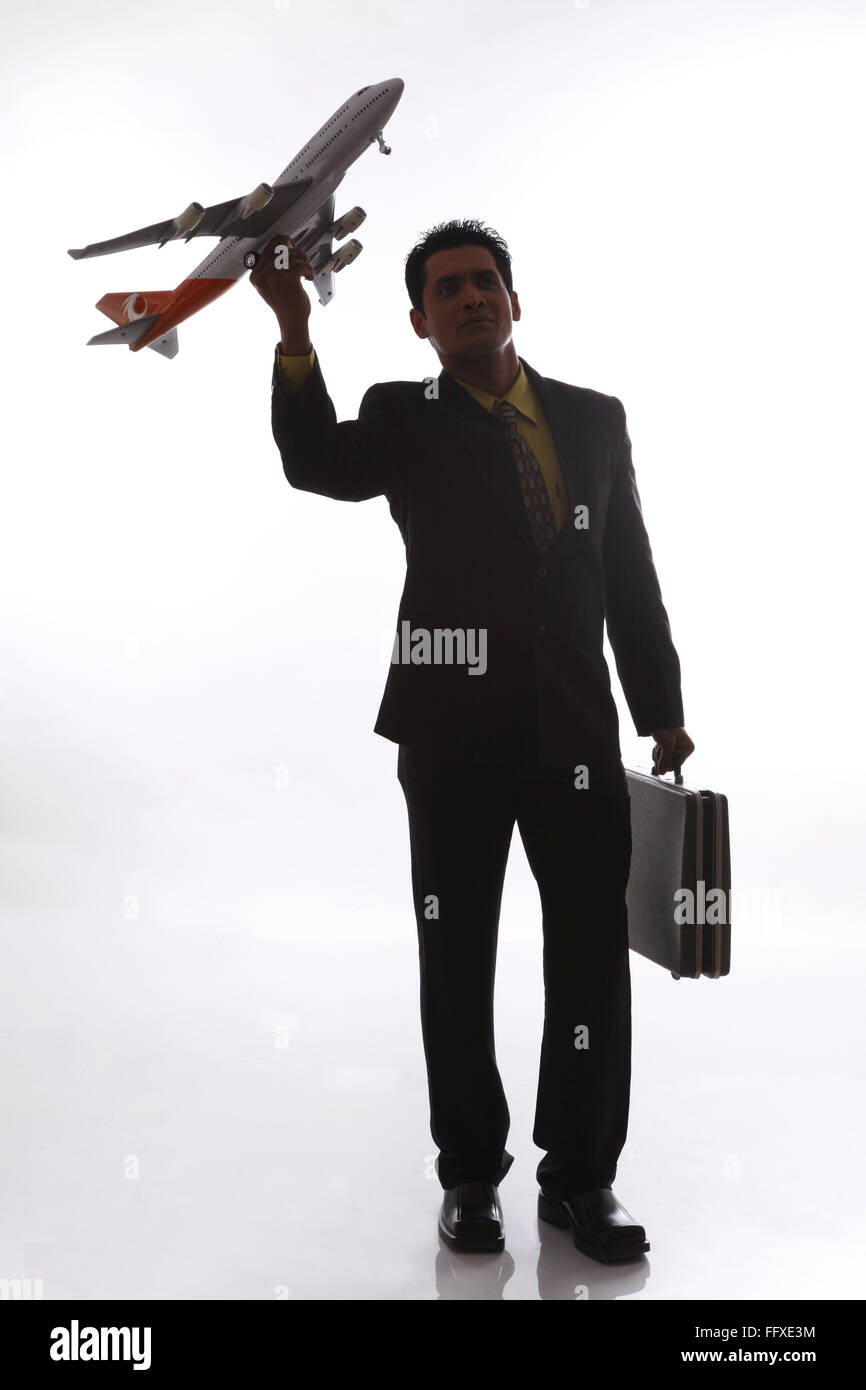 Businessman in silhouette holding passenger aeroplane in flying angle in one hand and briefcase in other hand MR#703T,NO PR Stock Photo