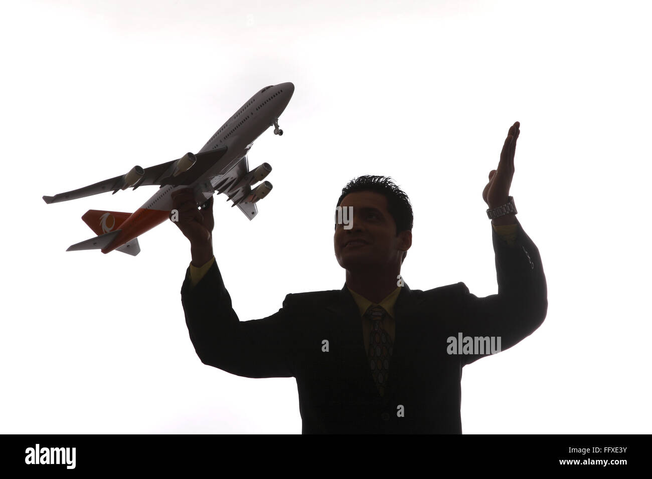 Businessman in silhouette holding passenger aeroplane in flying angle in one hand and raised other hand MR#703T,NO PR Stock Photo