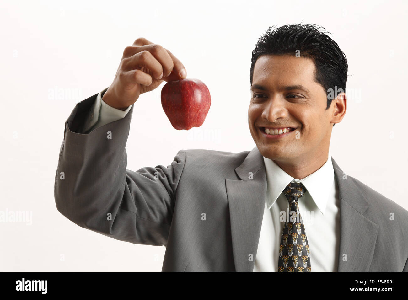 Businessman holding red apple in index finger with thumb of right hand