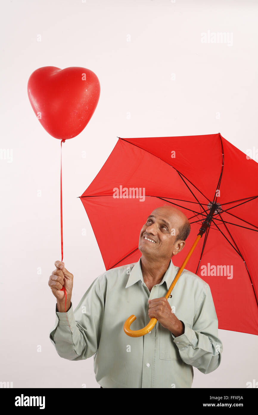 Old man looking upwards at heart shape gas balloon and holding red umbrella on shoulder MR#703I Stock Photo