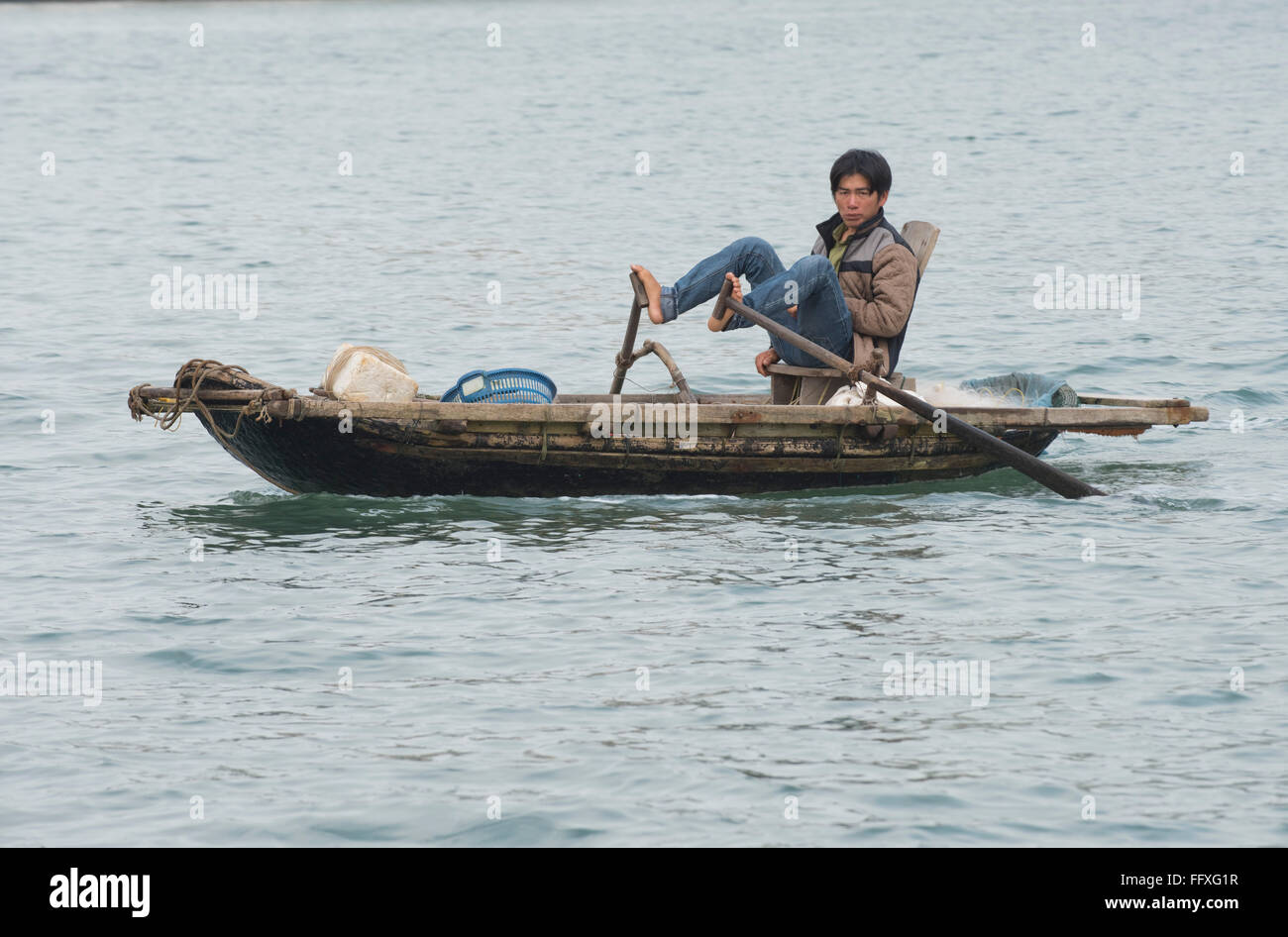 A small rowing boat used for fishing and transport, man traditionally using his feet to row, Halong Bay, Vietnam Stock Photo