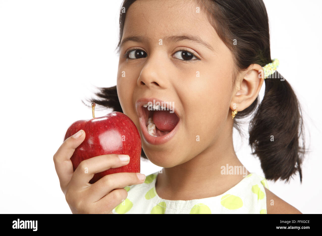 Eight year old girl holding red apple in one hand and thinking of
