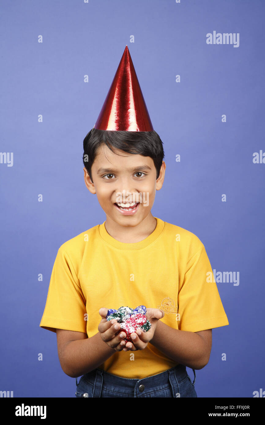 Ten year old boy holding chocolates in both hands wearing cone shaped
