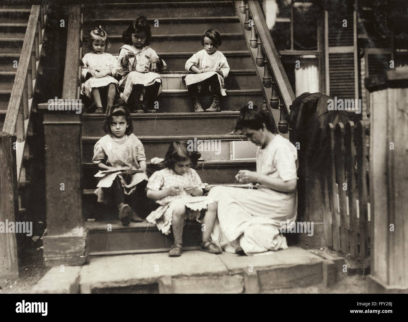 HINE: HOME INDUSTRY, 1912. /nA woman with a group of young girls working on garment tags on a tenement stoop in Roxbury, Massachusetts. Photograph by Lewis Hine, August 1912. Stock Photo