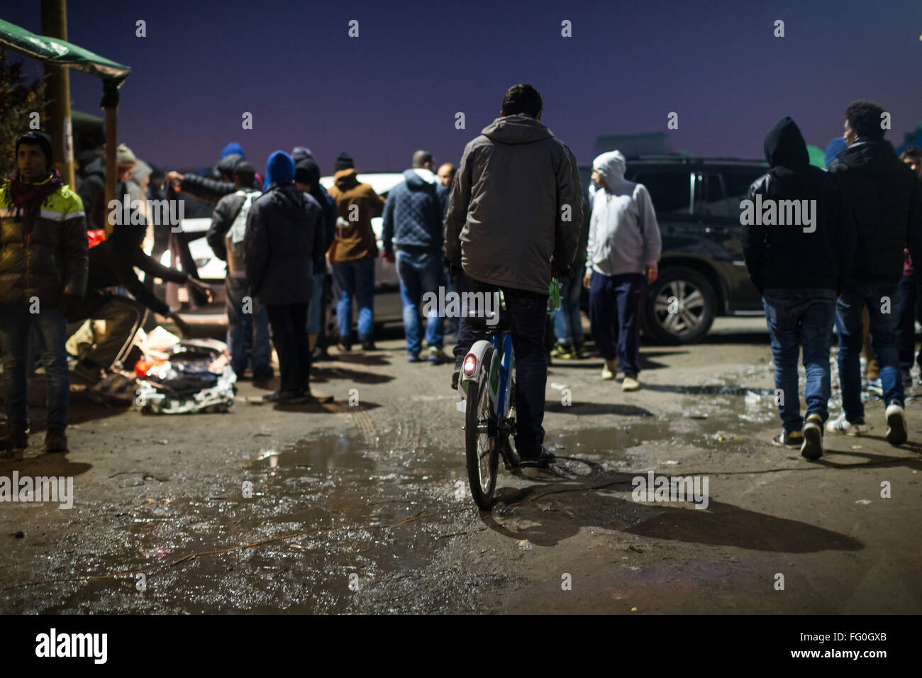 A refugee cycles through the mud at night in the Jungle Refugee Camp, Calais France Stock Photo