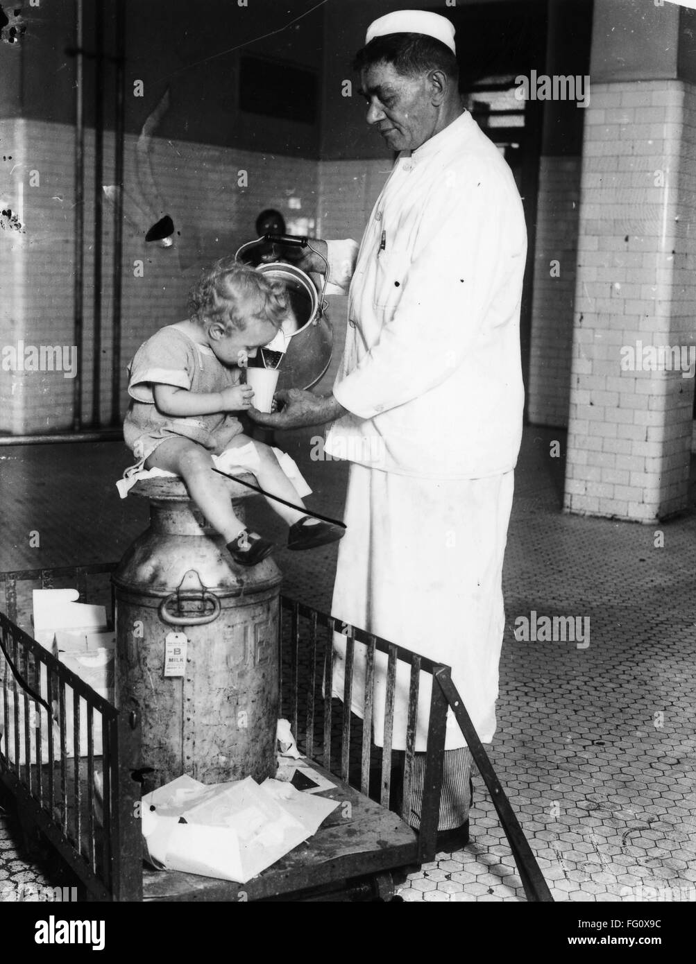 ELLIS ISLAND MILKMAN, 1925. /nA milkman pouring milk for a young