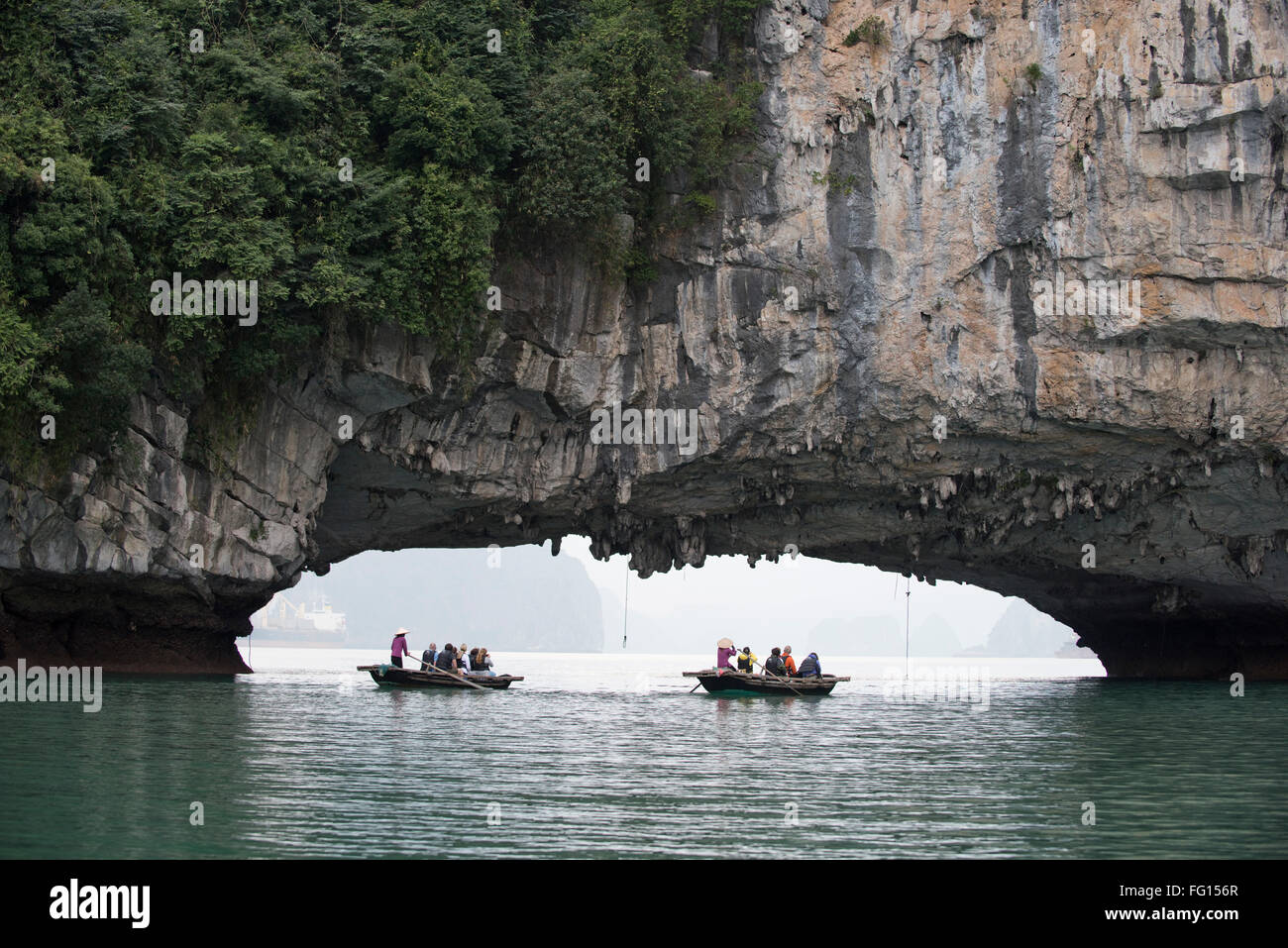 Tourist boats  rowing close to a tunnel cut by the sea in a limestone karst on Halong Bay in Northern Vietnam Stock Photo