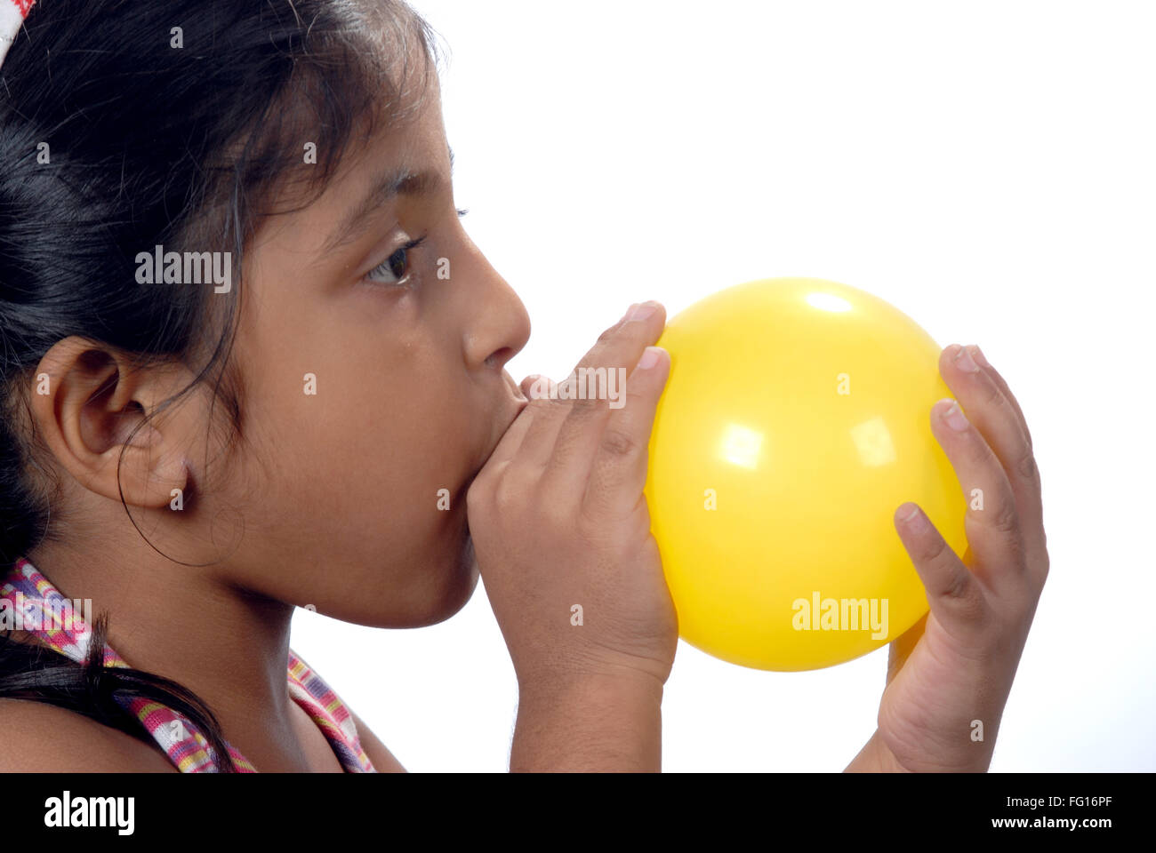 South Asian Indian six year old girl blowing yellow color balloon from mouth MR#364 Stock Photo