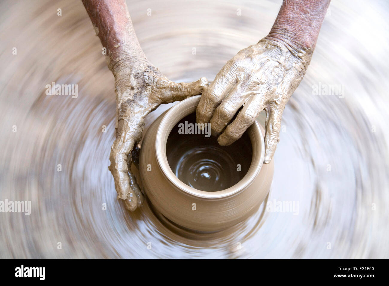 Pottery , artist muddy hands making clay pot giving shape on spinning wheel , semi urban village Dilwara Udaipur Rajasthan Stock Photo