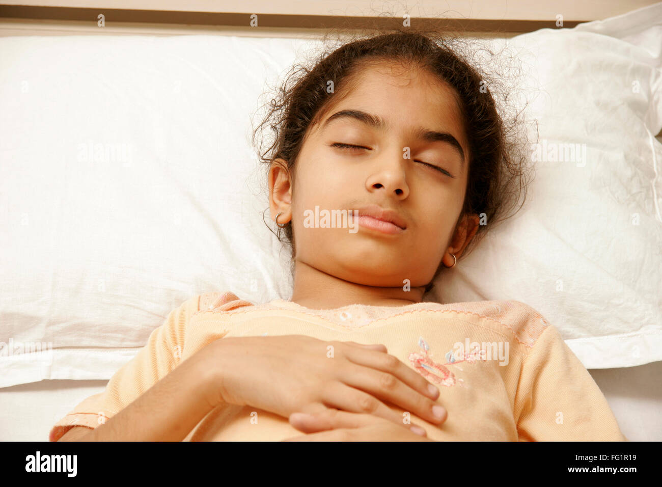 South Asian Indian 9 years old girl wearing peach colour nightwear having sound asleep on bed MR#191 Stock Photo