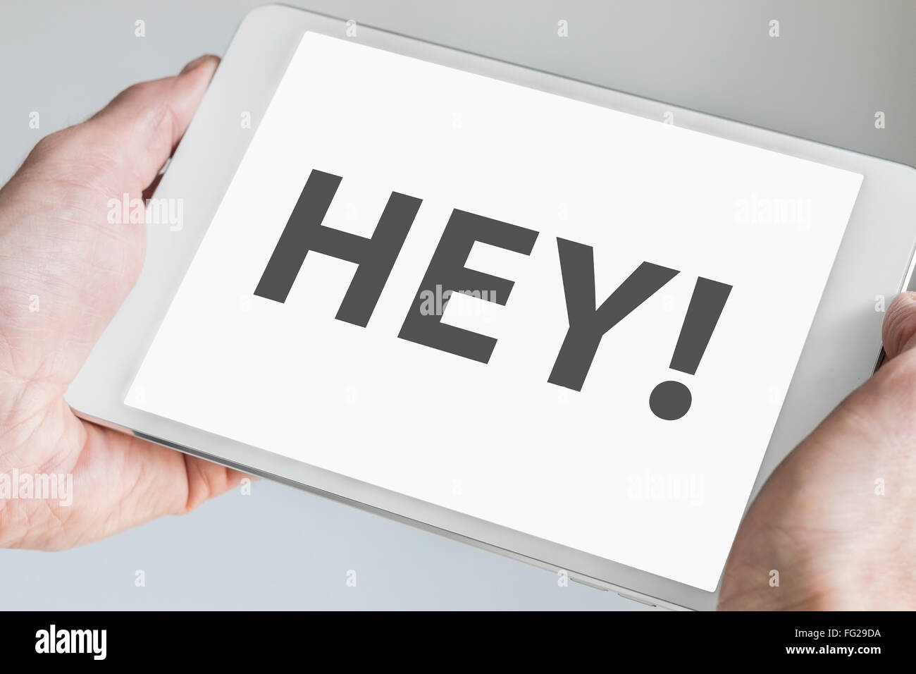 Hey text displayed on touch screen of a modern tablet computer. Hands holding mobile device to interact with a social network Stock Photo