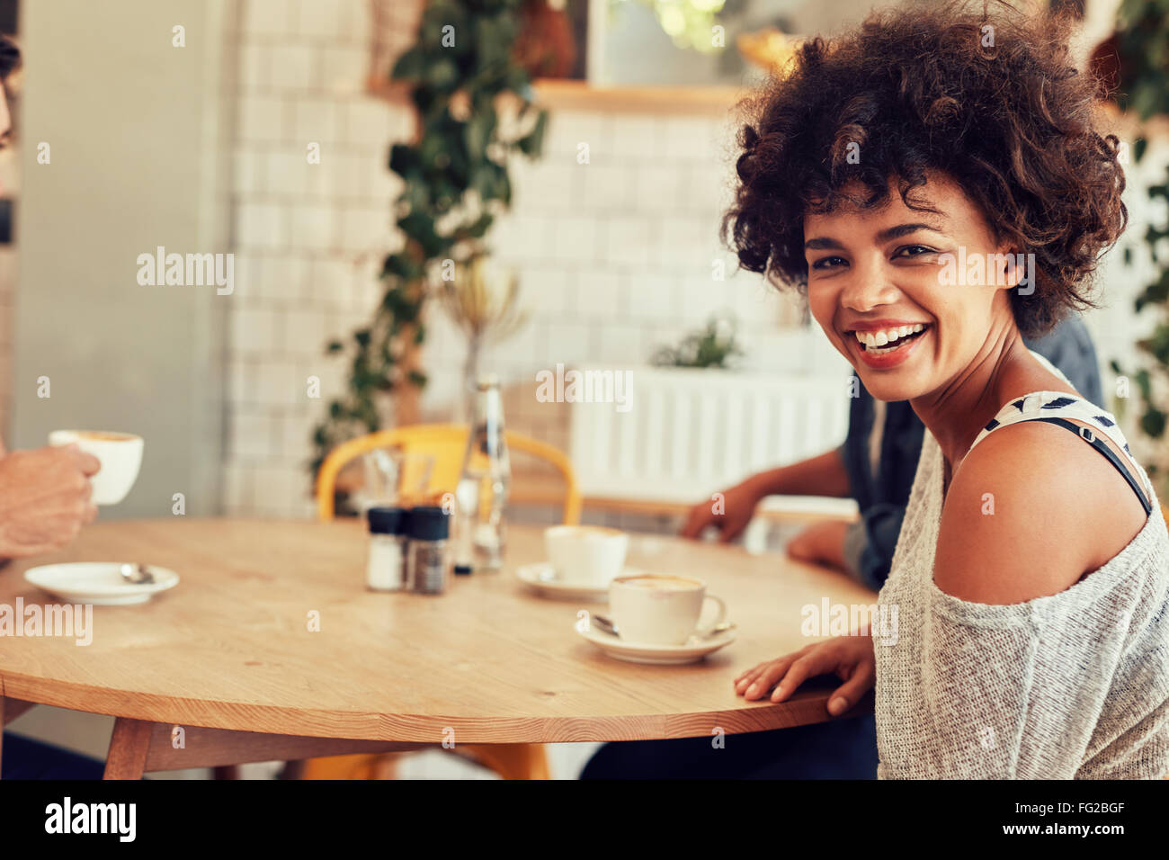 Portrait of cheerful young woman sitting at a cafe table with friends in background Stock Photo