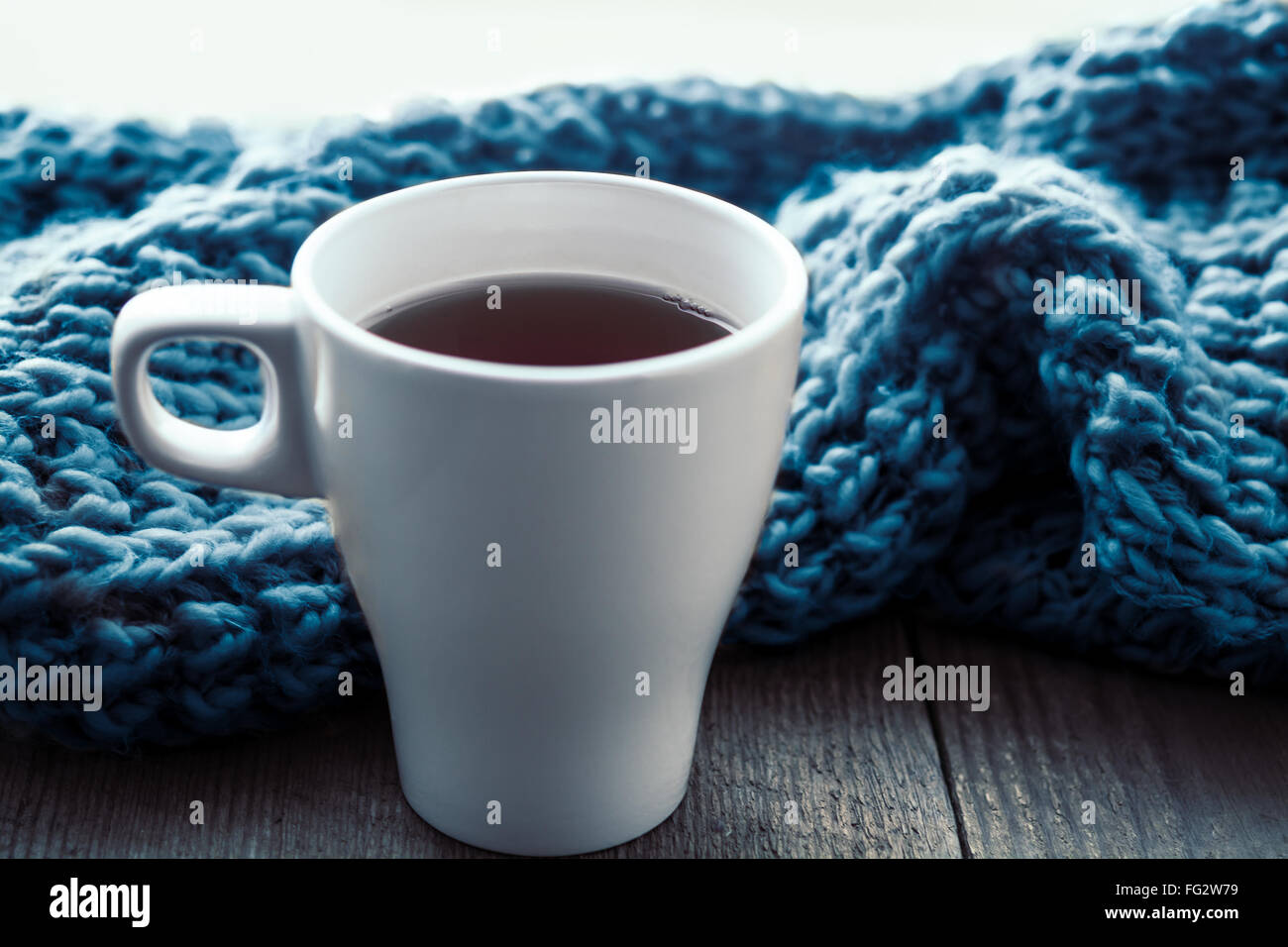 White cup of tea and scarf on old wooden desk. Selective focus, toned Stock Photo
