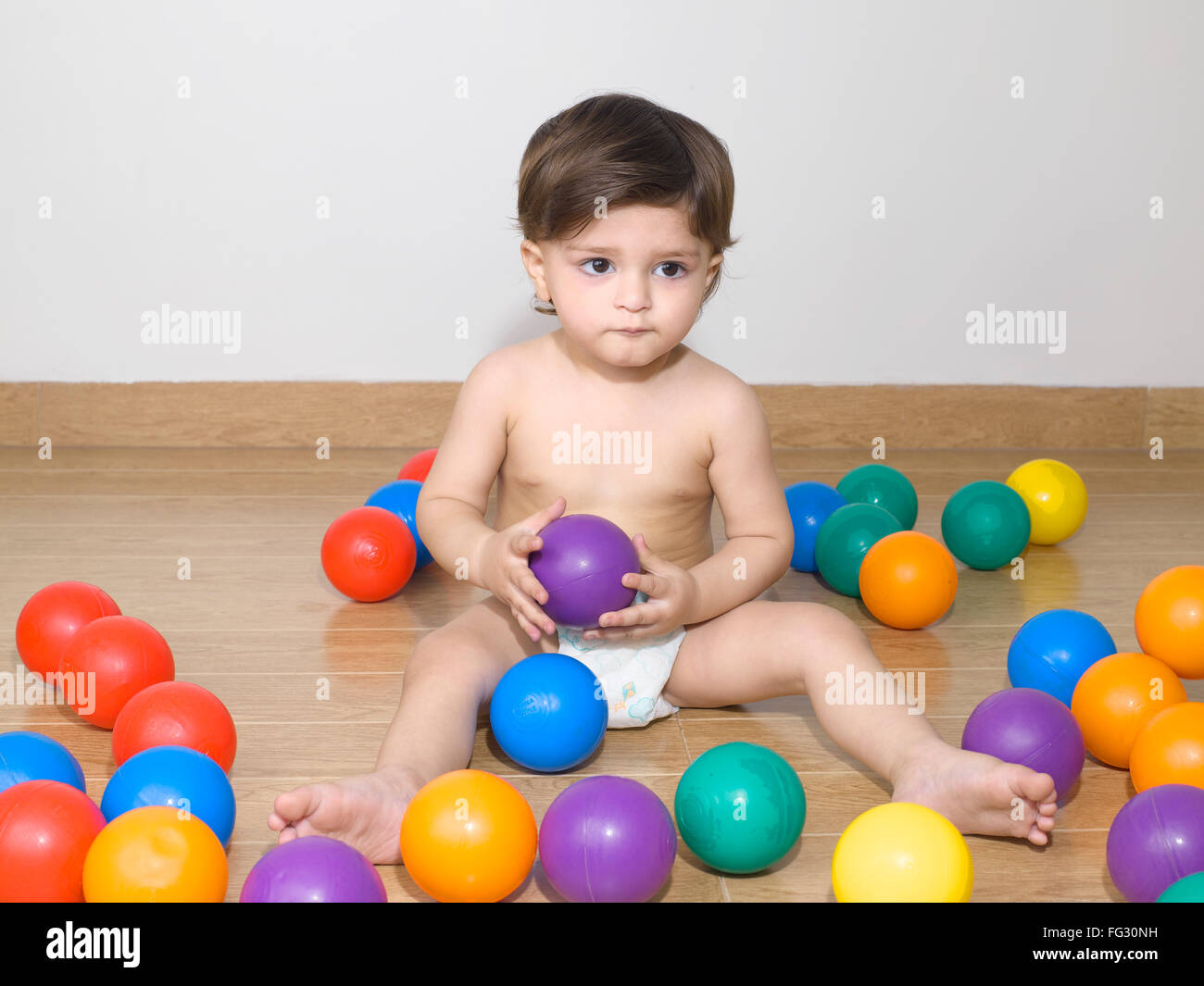 Baby wearing diaper playing with colourful balls ; MR779N Stock Photo