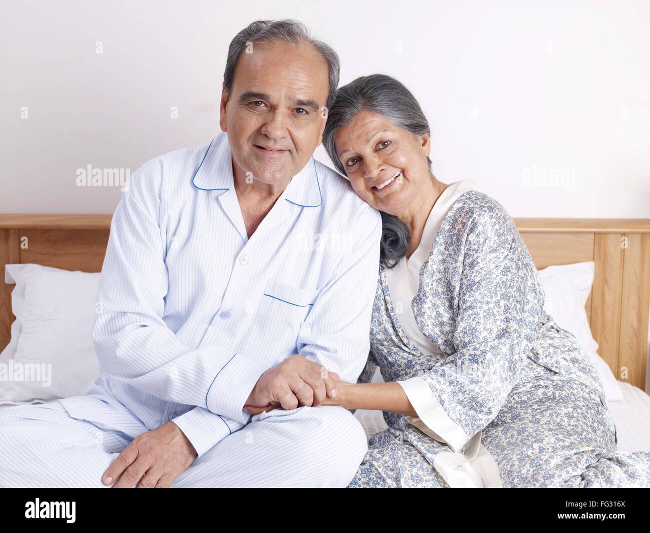 Old couple holding hands sitting close to each other on bed MR#702T,702S Stock Photo