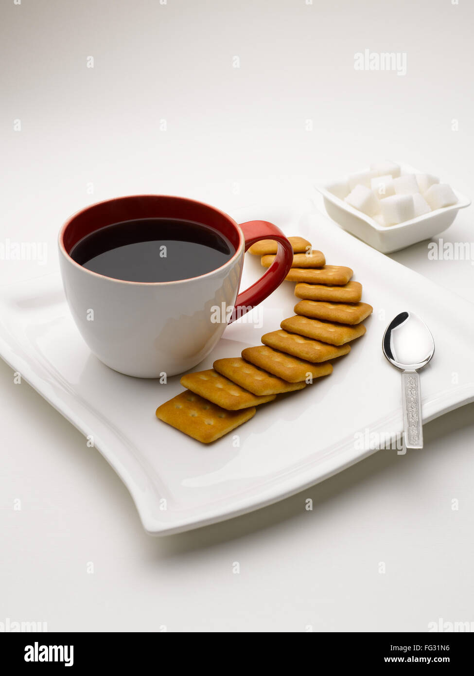 mug of black tea in serving plate with sugar cubes and biscuits India Stock Photo