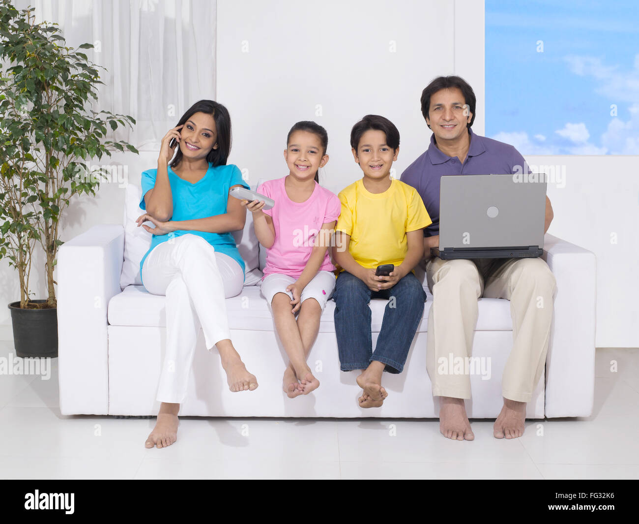 Woman and son using mobile while man using laptop and daughter with remote MR#779P ; MR#779Q ; MR#779R ; MR#779S Stock Photo