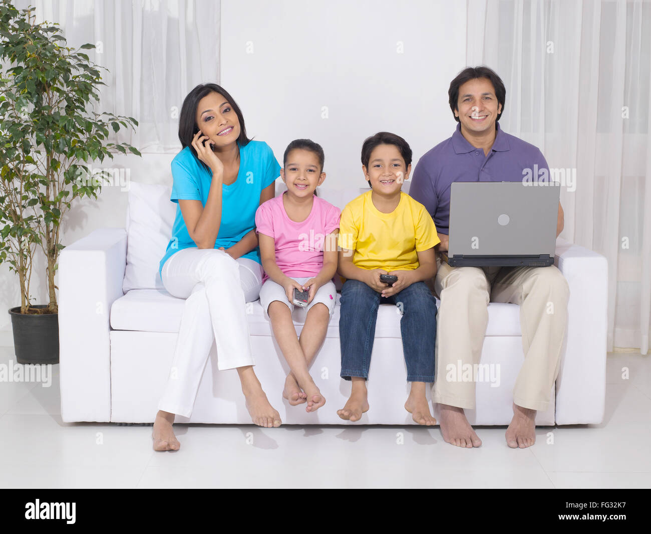 Woman and son using mobile while man using laptop and daughter with remote MR#779P ; MR#779Q ; MR#779R ; MR#779S Stock Photo