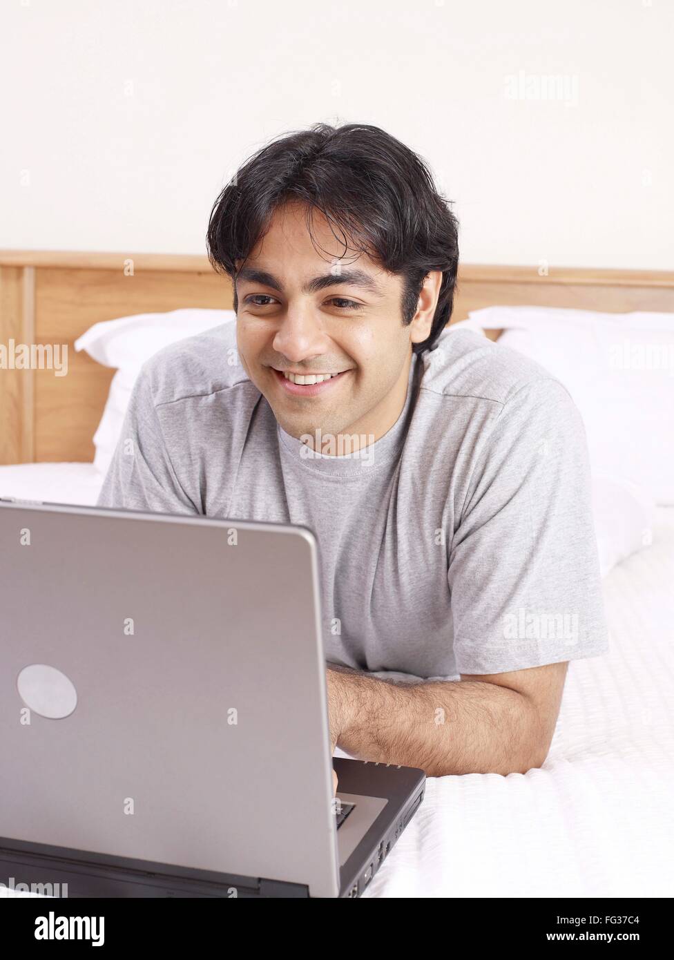 Young man operating laptop laying on bed MR#702V Stock Photo