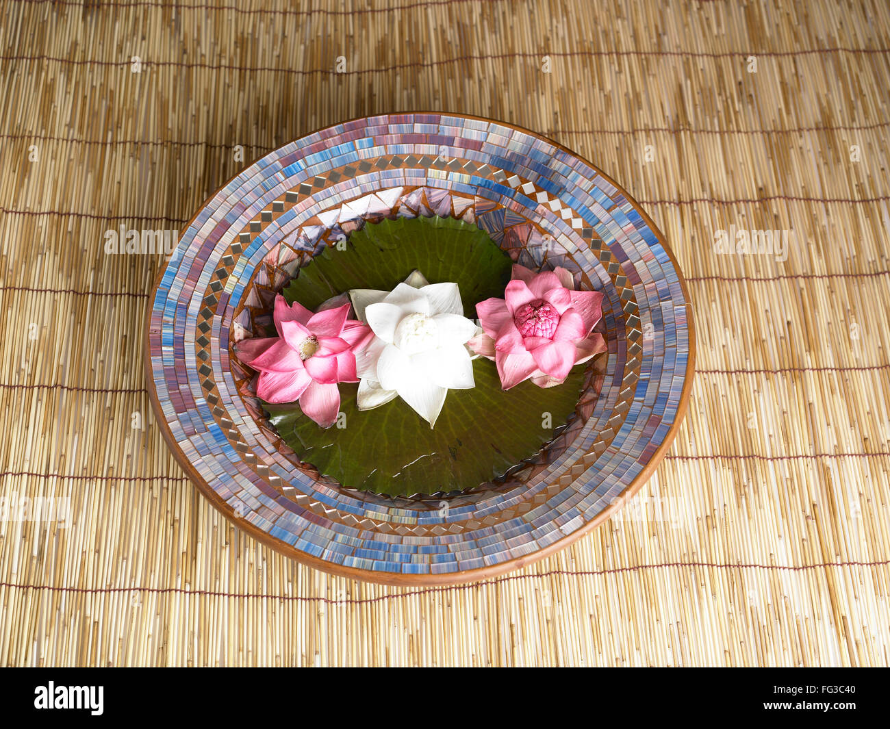 Two red and one white lotus flower kept in plate on the wooden mat Stock Photo