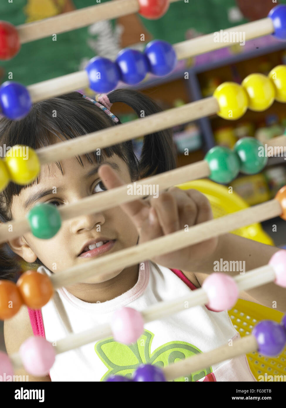 South Asian Indian girl sitting in front of abacus and calculating beads sliding on wires in nursery school MR Stock Photo