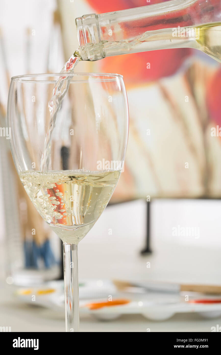 White wine pouting into wine glass with painting in background Stock Photo