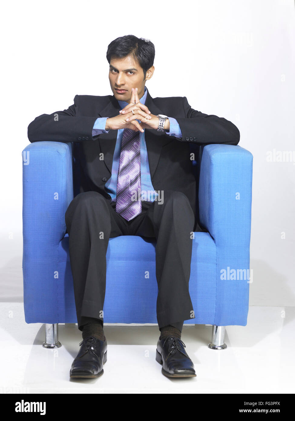 South Asian Indian executive man sitting on blue sofa MR Stock Photo