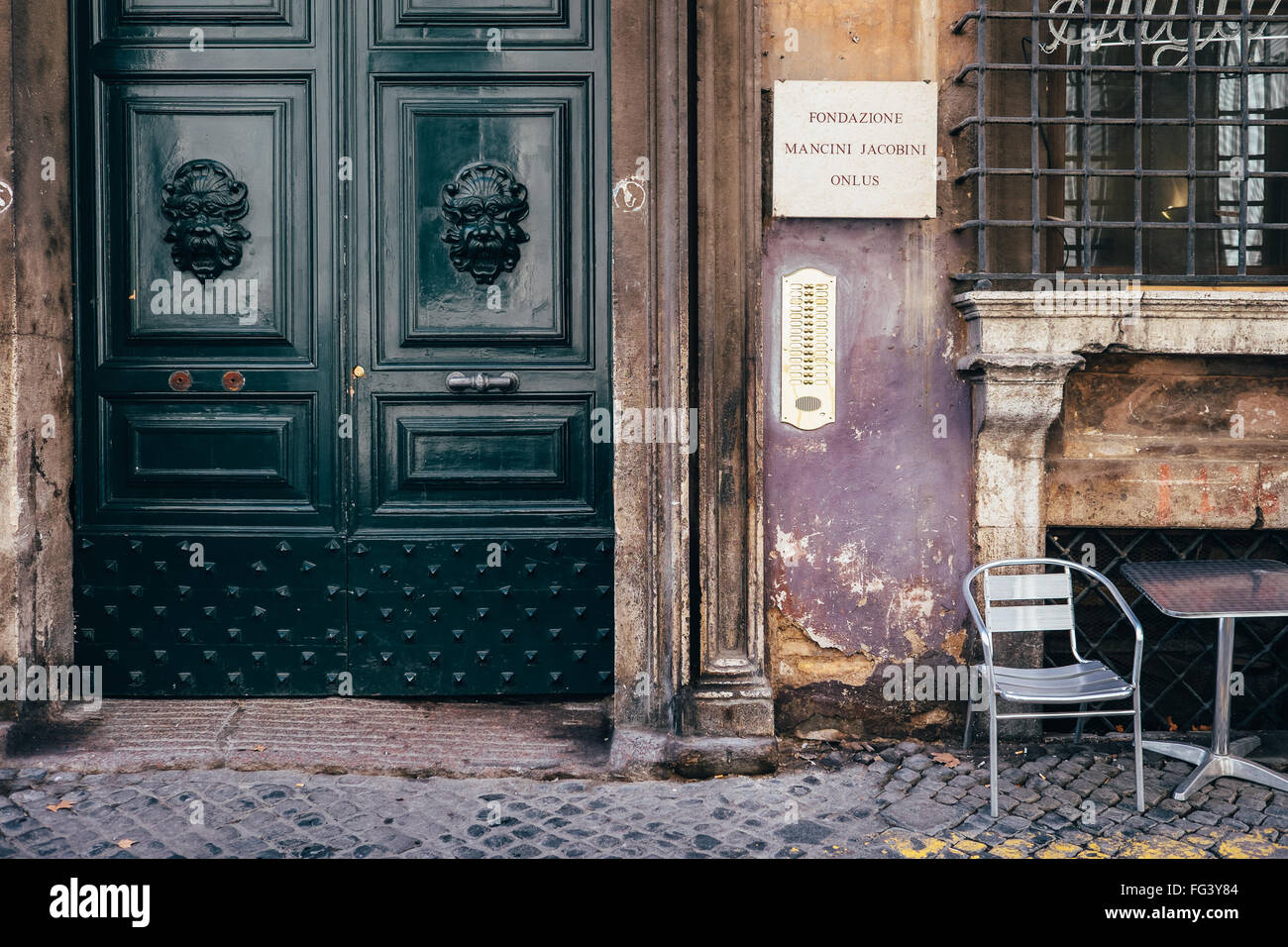 A worn wall and elegant door with a silver chair positioned for people-watching in Via Giulia, Rome, Italy Stock Photo