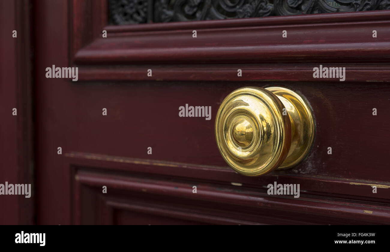 Shiny brass metal doorknob on maroon red wooden entrance door Stock Photo